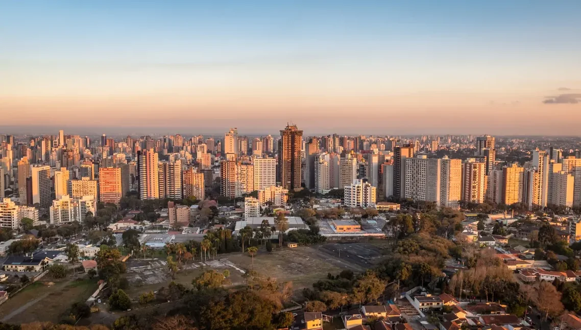 Panorama de cidade grande ao entardecer, com parque arborizado à frente